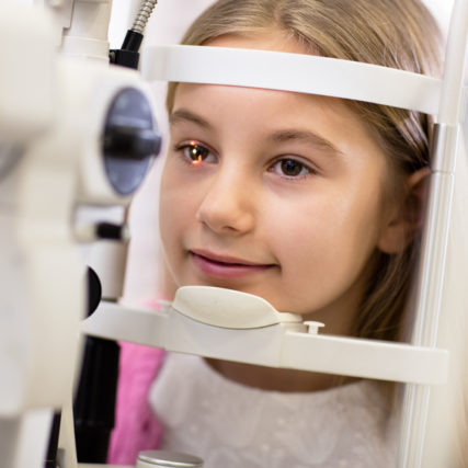 Pretty girl look at ophthalmoscope in eye clinic